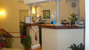 A reception area with a marble counter, a chandelier, and a clock on the wall. - Hotel Demetra Capitolina (Rome)