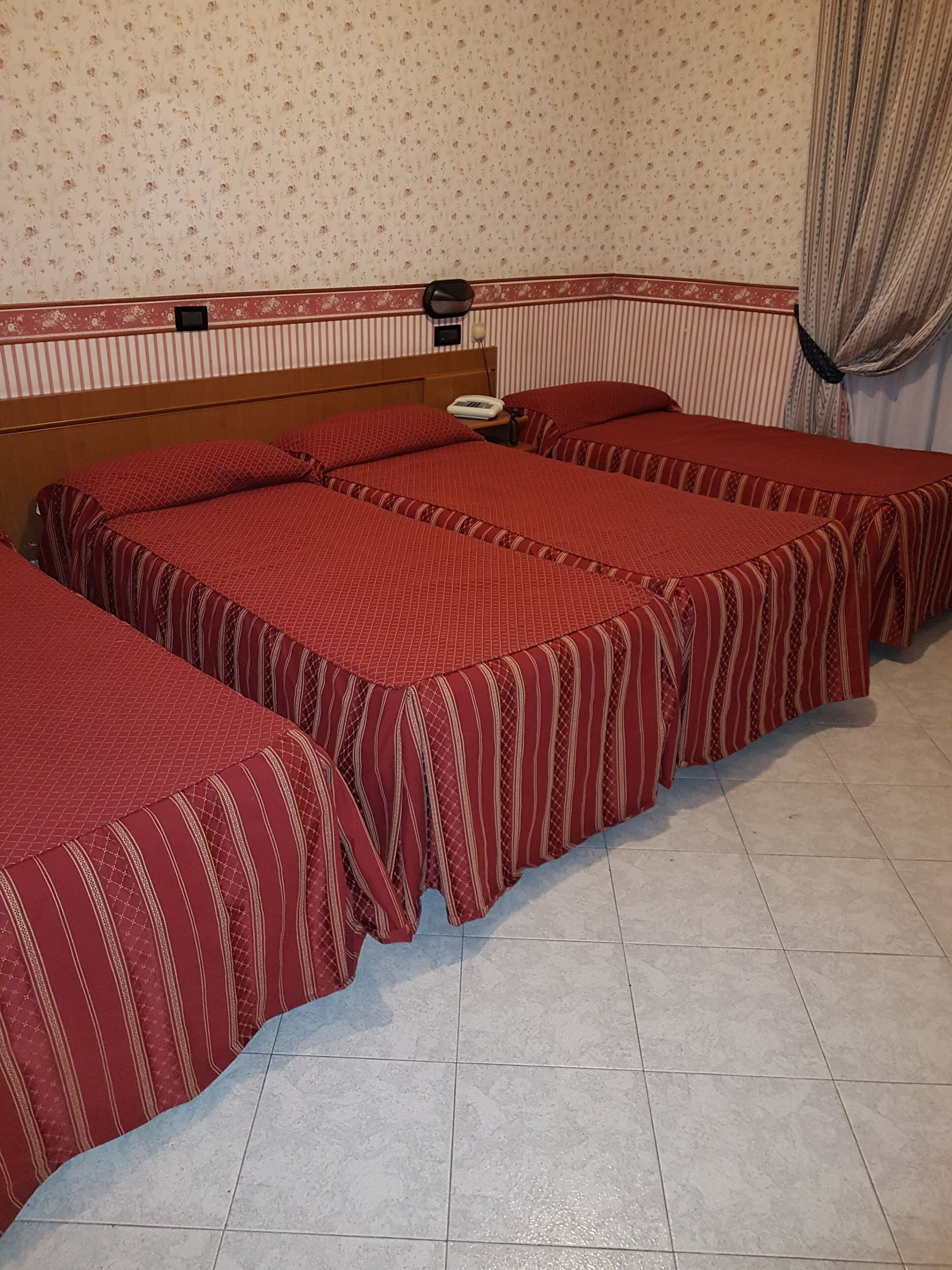 Camera d'albergo con due letti, una testiera in legno, un comodino con una lampada e una parete decorata.