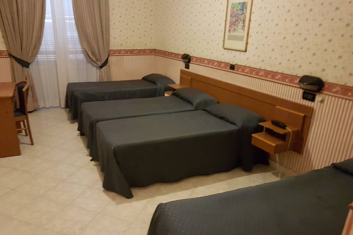 A hotel room with three single beds, a wooden desk, and a chair.