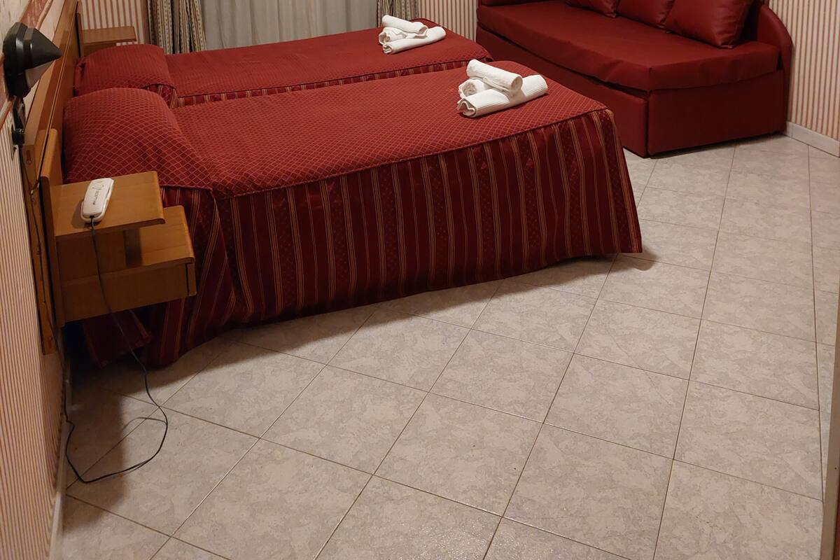 A hotel room with a bed, a red sofa, a ceiling fan, and a window with curtains.