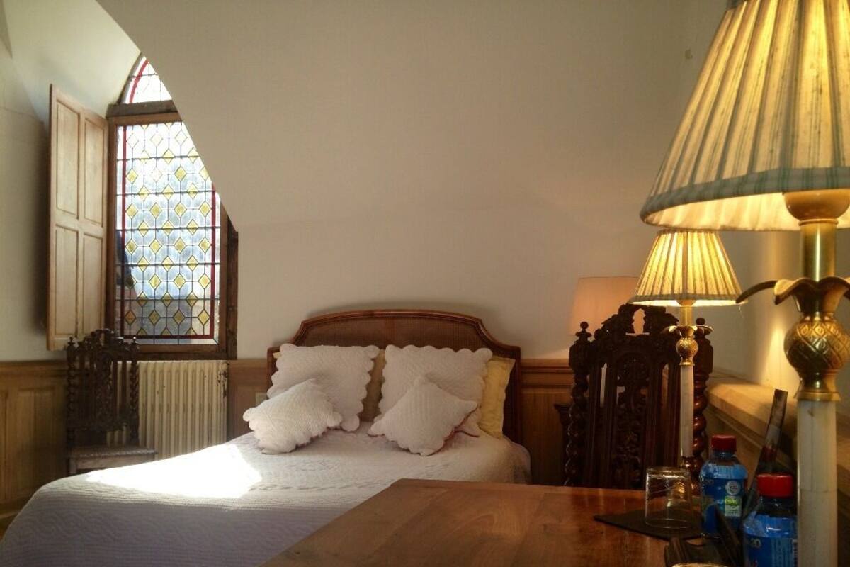Een slaapkamer met een houten bed, nachtkastje, lamp en een raam met glas-in-lood.