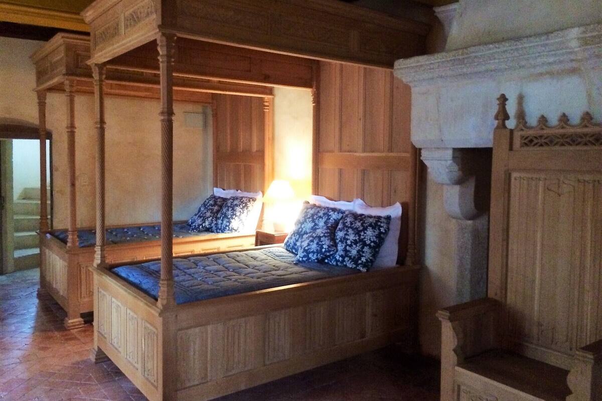 Een hemelbed met houten baldakijn, twee kussens en een nachtkastje.