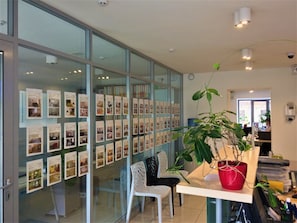 A modern office space with glass walls displaying photographs, a white chair, a red potted plant, and a desk with a laptop. - Partner Guest House Shota Rustaveli (Kyiv)