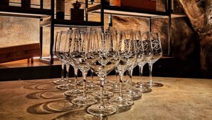 A bar area with multiple wine bottles on shelves and a row of empty wine glasses on a table. - Hotel America (Locarno)
