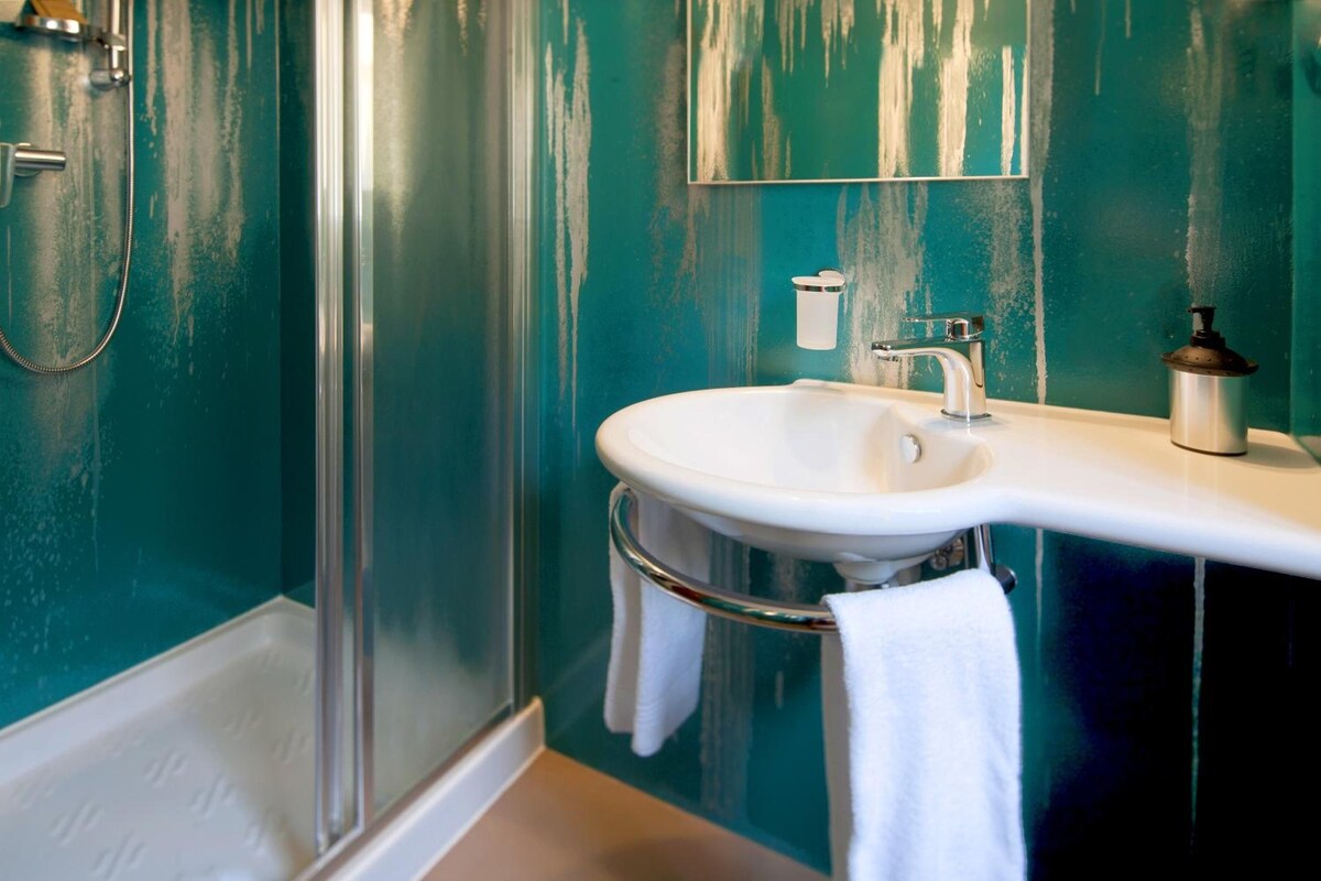 A bathroom with a white sink, a mirror, a handheld showerhead, and a towel hanging on a rack.