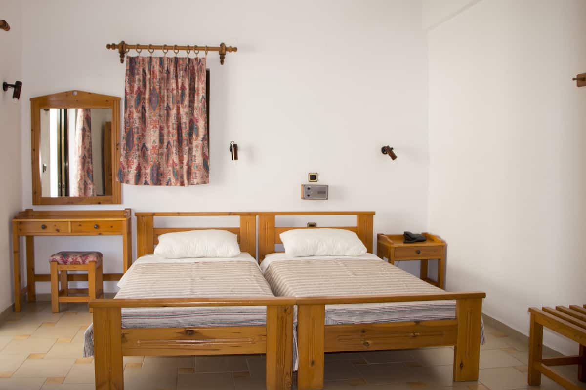 A bedroom with a wooden bed, a desk, a chair, a mirror, and a curtain.