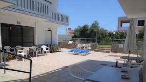 An outdoor patio area with white plastic chairs and tables, a blue pool, and a stone wall. - Popi (Chania)