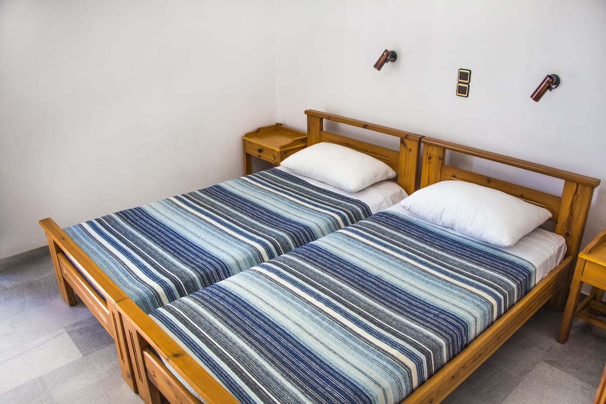A double bed with a striped bedspread, wooden headboard, two bedside tables, and a wall-mounted light fixture.