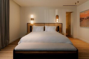 A hotel room with a large bed, a headboard with integrated lighting, a painting on the wall, and a wooden floor. - Hotel Capri (Sitges)