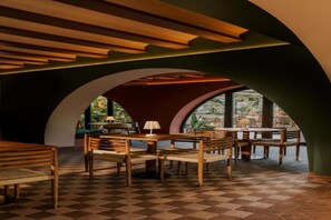 An indoor dining area with checkered flooring, wooden furniture, and a view through large windows. - Hotel Capri (Sitges)