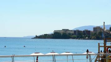 A beach with umbrellas and lounge chairs, a lifebuoy, and a view of buildings across the water.