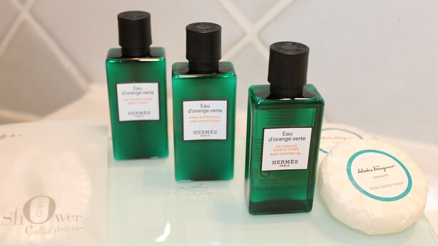Trois flacons de lotion pour le corps de couleur verte et un pain de savon, le tout posé sur une surface blanche.
