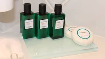 Tre flaconi di lozione corpo Hermes color verde e due saponette bianche su un ripiano in vetro.