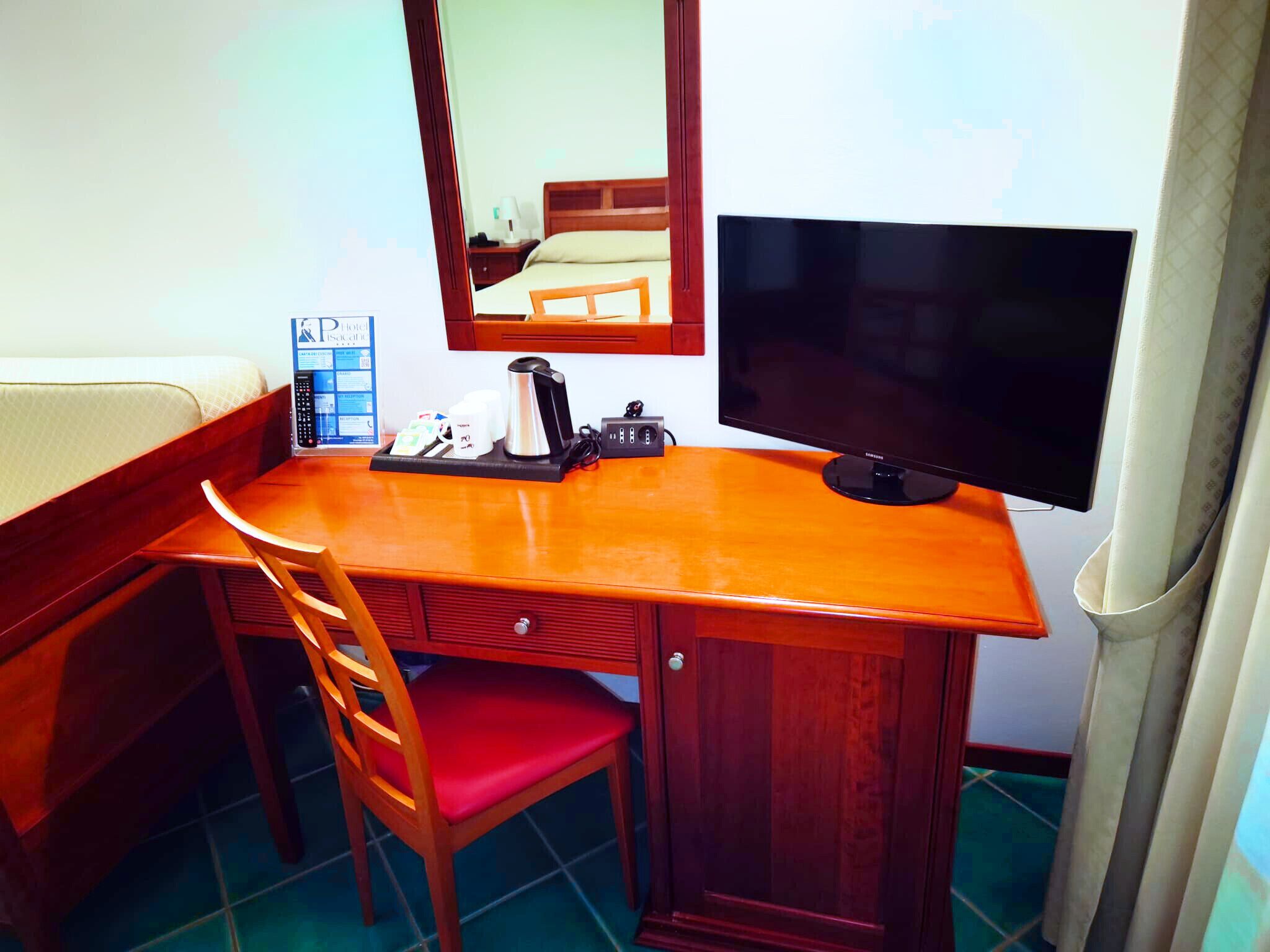Une chambre d’hôtel de taille modeste, avec un bureau en bois, une chaise rouge, un téléviseur et un miroir.