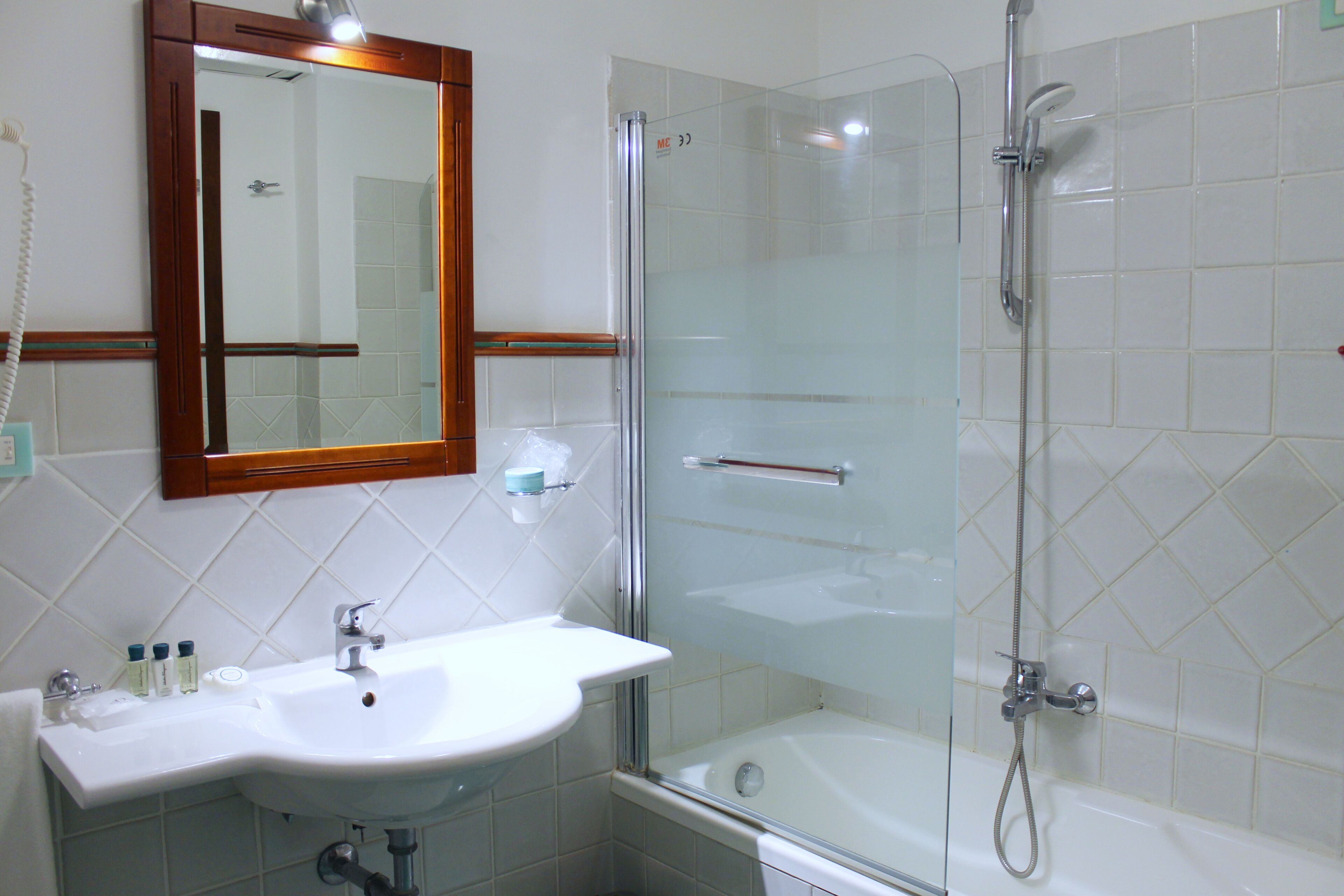 Une salle de bain avec une douche à parois de verre, un lavabo blanc avec un miroir au-dessus, et un sol carrelé.