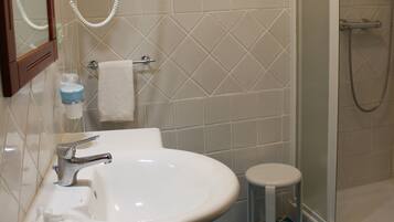A bathroom with a sink, mirror, towel rack, and a shower area.