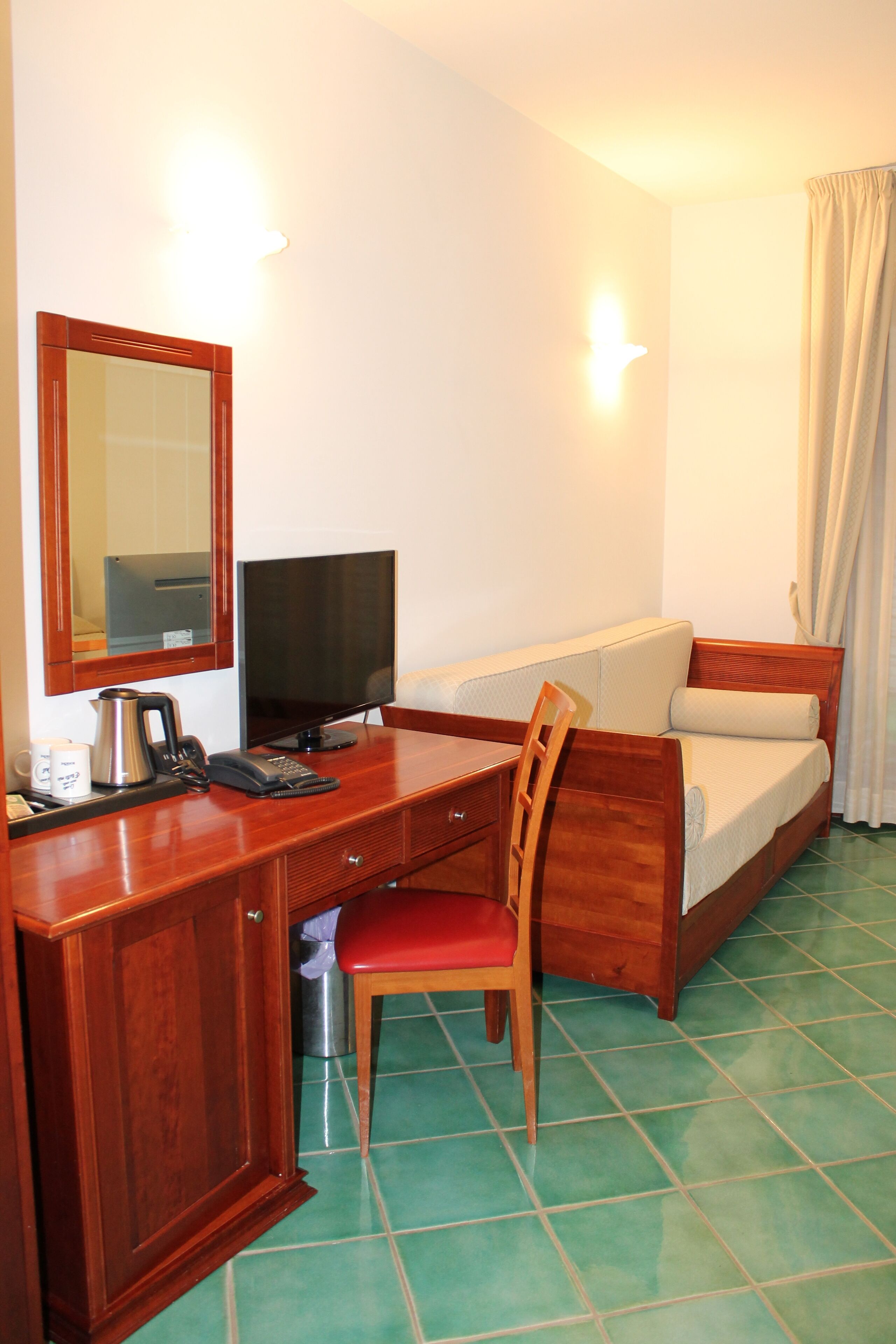 Une chambre d’hôtel avec un bureau en bois, une télévision, un lit et une chaise rouge.