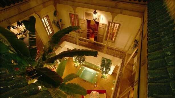 A high-ceilinged atrium with a central pool, a dining area with a red tablecloth, and a staircase with a balustrade.