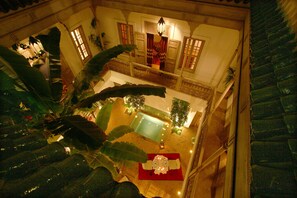 Um átrio amplo, com pé-direito alto, possui uma piscina central, uma área de refeições com toalha vermelha e uma escadaria com balaústres.