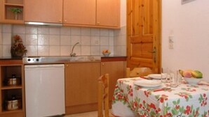 Una cuina compacta amb armaris de fusta, un refrigerador blanc i una taula de dinar preparada amb plats i un bol de fruita.