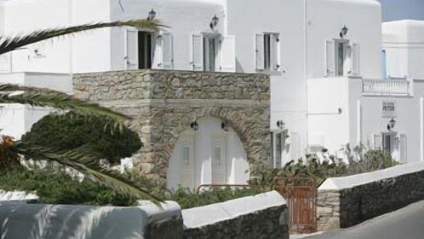 Edifici blanc amb arcada de pedra, un jardí petit i una zona pavimentada al davant.