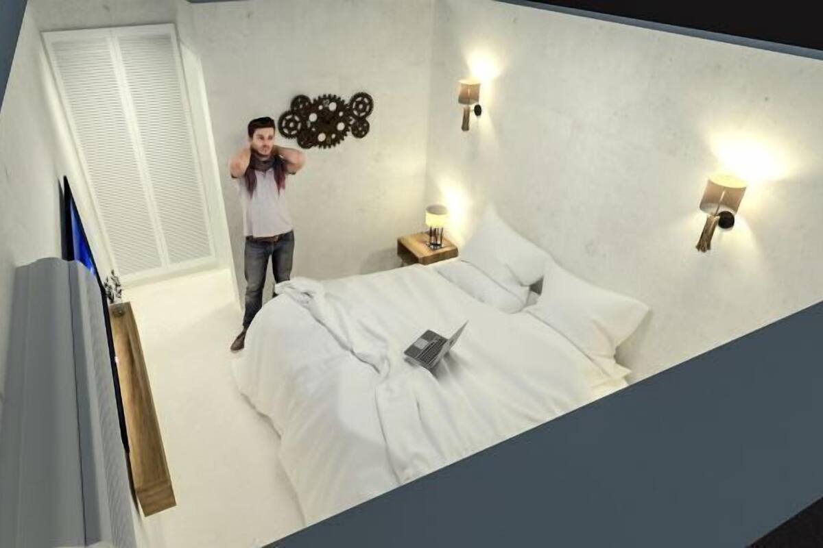 A bedroom with a bed, a nightstand with a lamp, a wall-mounted clock, and a window with blinds.