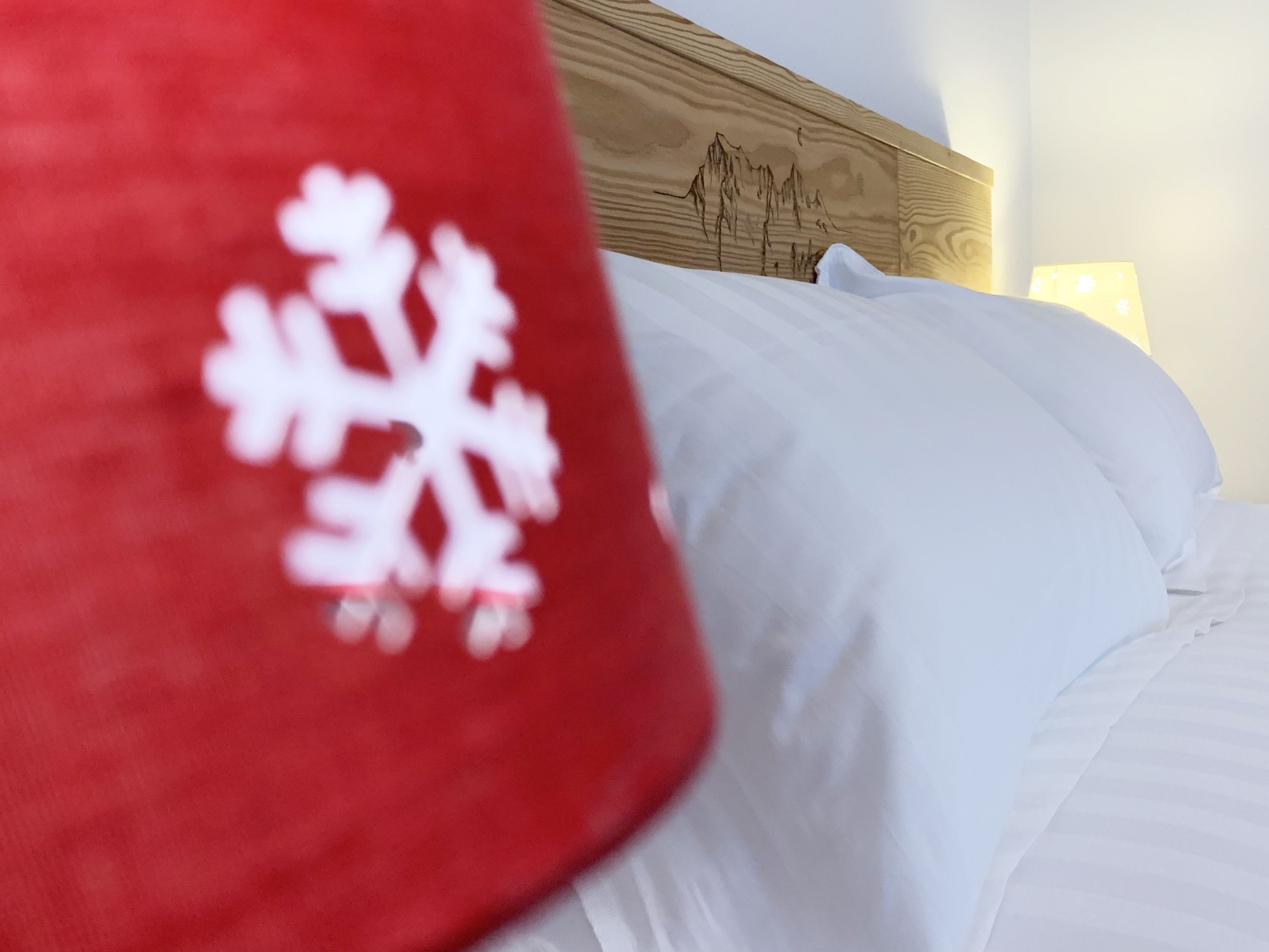 Una cama con ropa blanca y una almohada roja con un diseño de copo de nieve blanco.