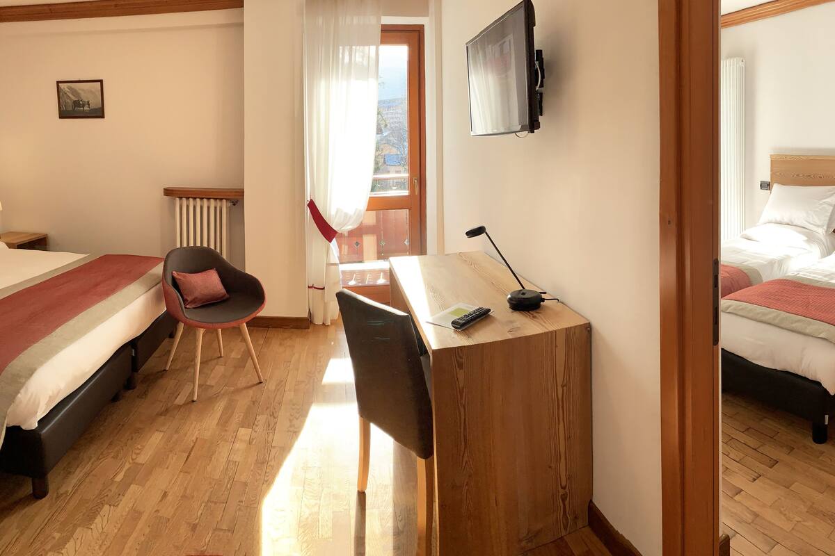A hotel room with two beds, a desk with a computer, a chair, and a window with curtains.