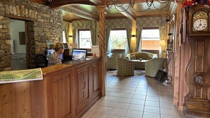 Un área de recepción con un escritorio de madera, una recepcionista y una computadora. Hay un sofá y un reloj en la pared.
