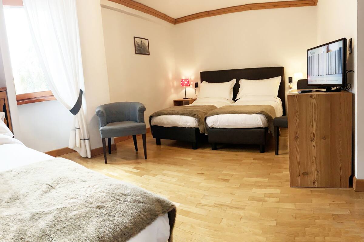 A bedroom with a wooden headboard, a single bed, a double bed, a chair, a TV, and a nightstand with a lamp.