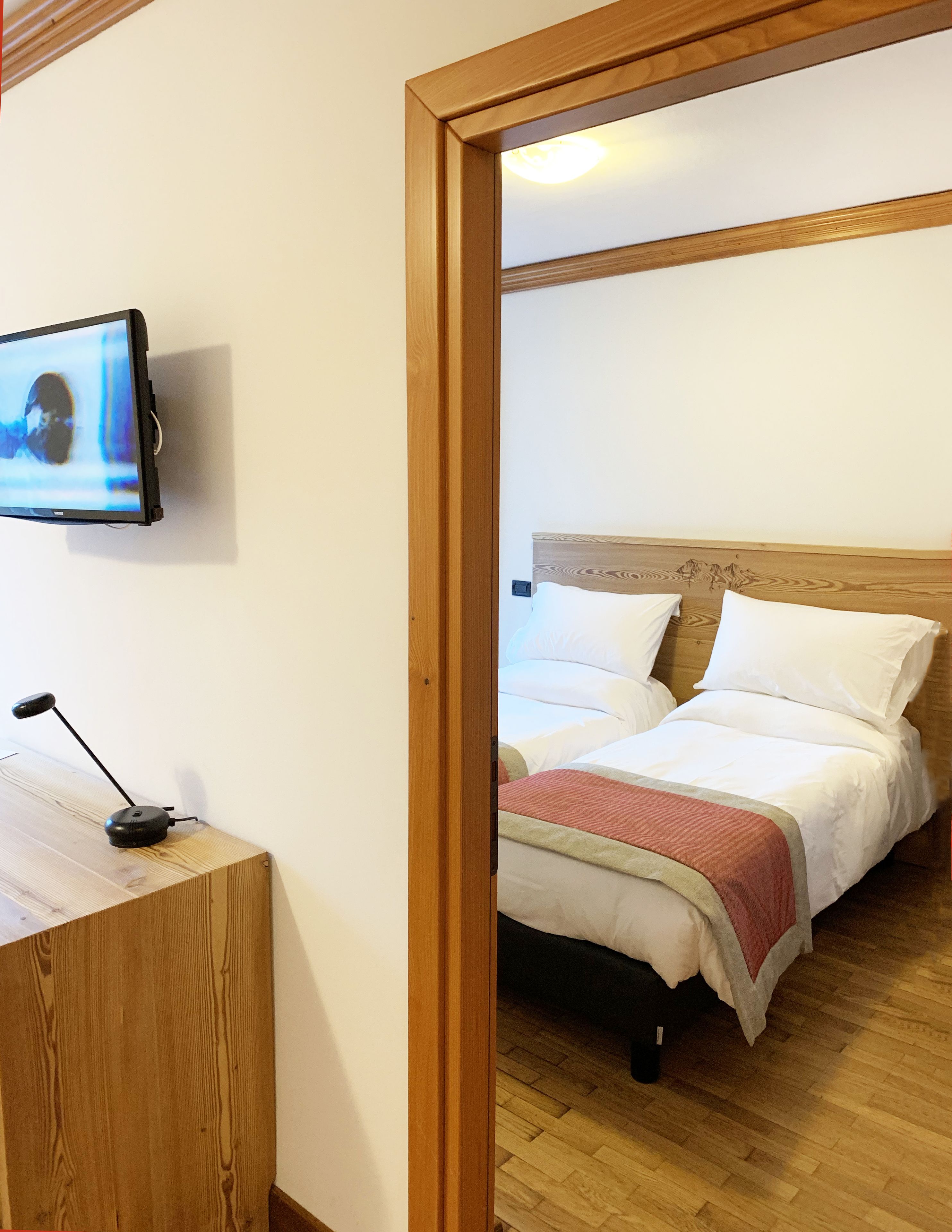 Una habitación de hotel con un escritorio de madera, un televisor montado en la pared y una cama con ropa blanca y una colcha roja.