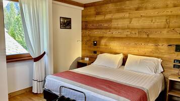 Un dormitorio con cabecera de madera, cama con ropa blanca, mesita de noche y ventana con cortinas.