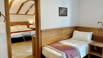 Una habitación con cabecera de madera, cama con manta roja y gris, mesita de noche con lámpara y un cuadro enmarcado en la pared.
