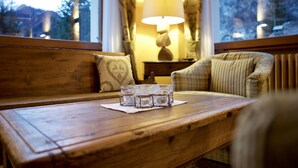 Un banco de madera con una mesa de vidrio al frente, una lámpara y vistas a árboles y montañas a través de una ventana.
