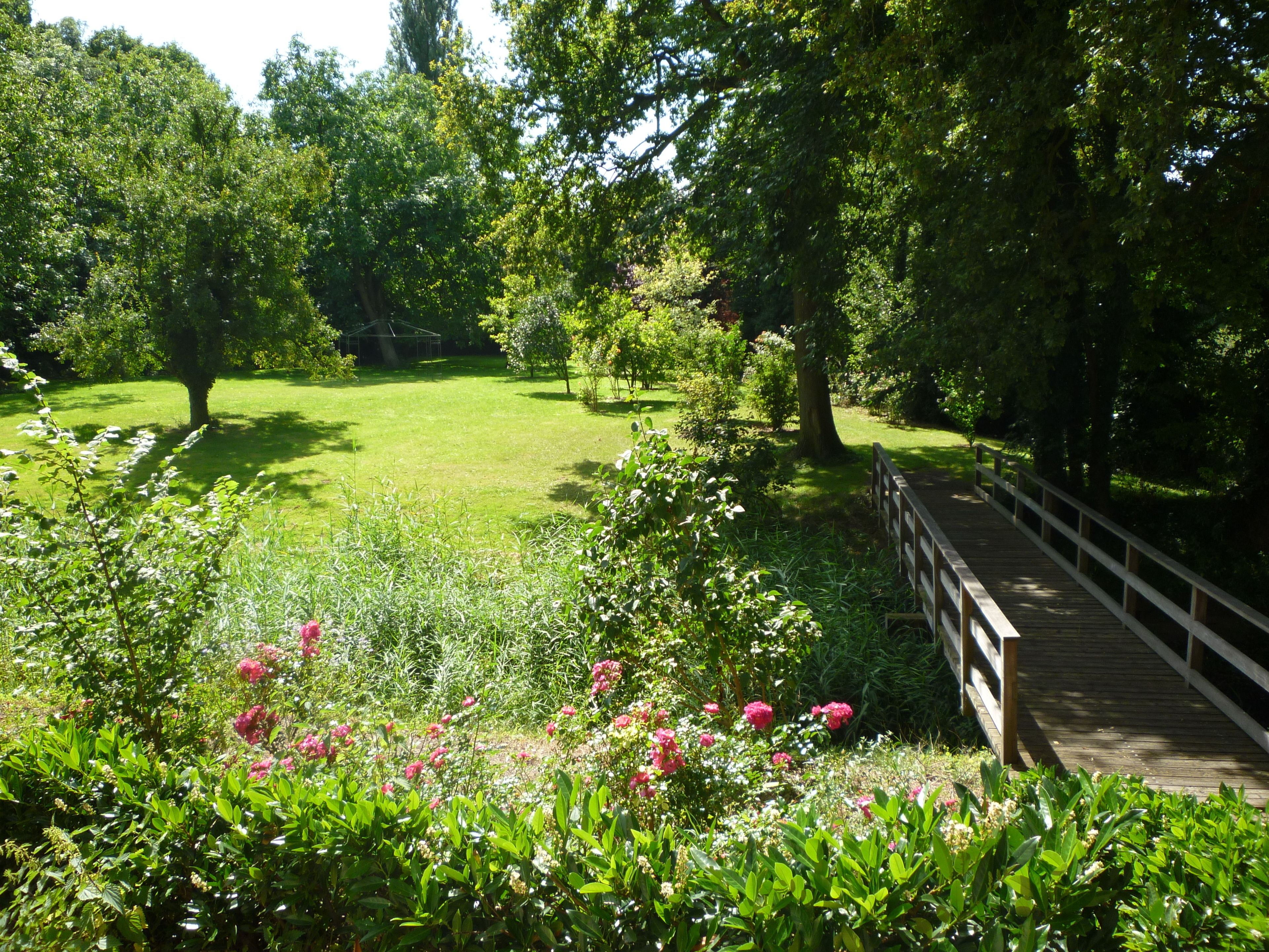 A garden with a wooden bridge, lush greenery, and flowering plants.