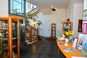 Um hall amplo com escada, balcão de recepção e uma vitrine com diversos objetos.