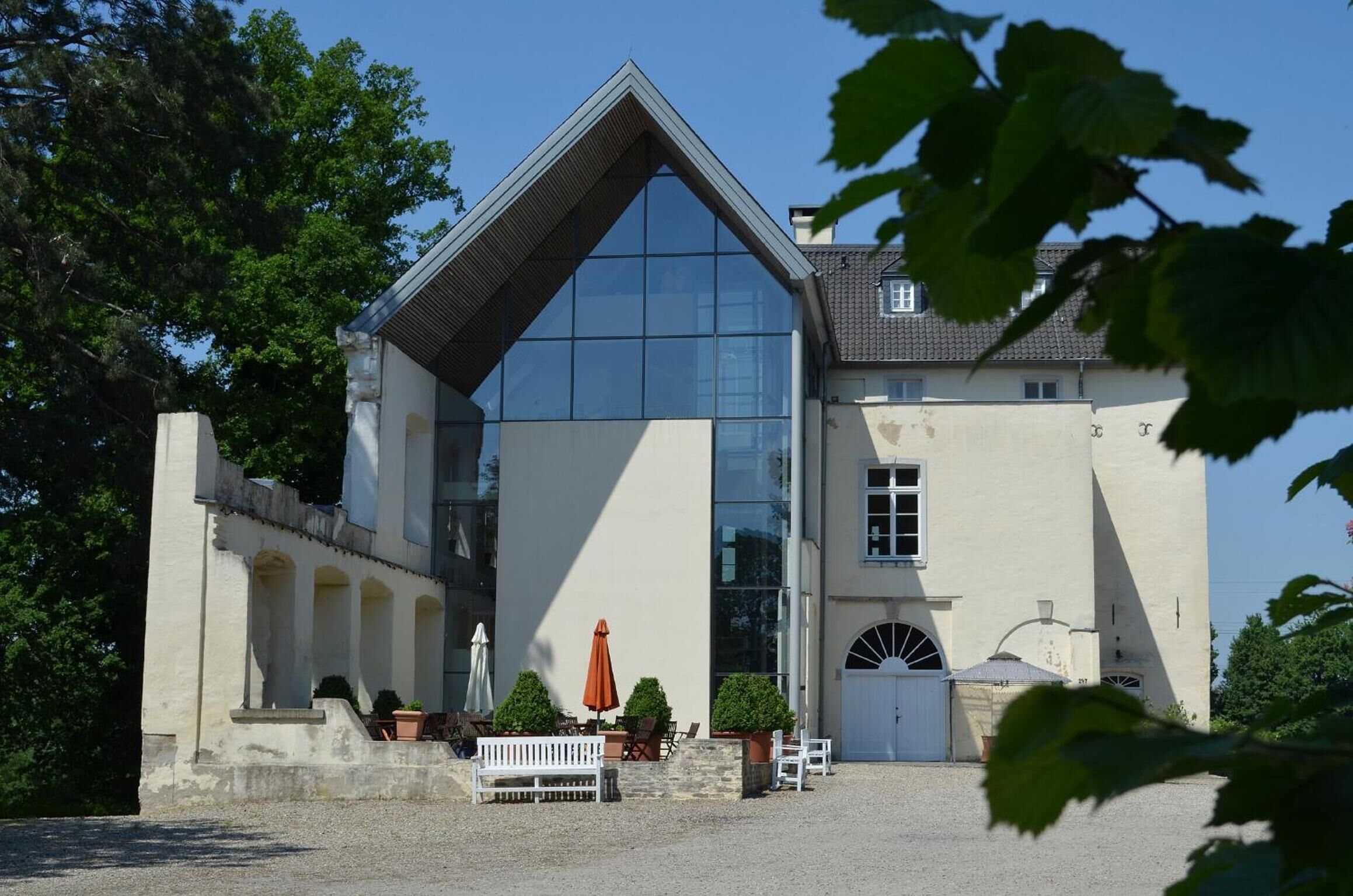 A building with a large glass facade, a pitched roof, and a courtyard with outdoor seating.