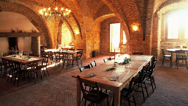 A spacious dining hall with brick arches, wooden tables, and chairs.