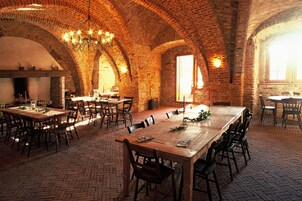 Uma sala de jantar ampla, com arcos de tijolo, mesas e cadeiras de madeira.
