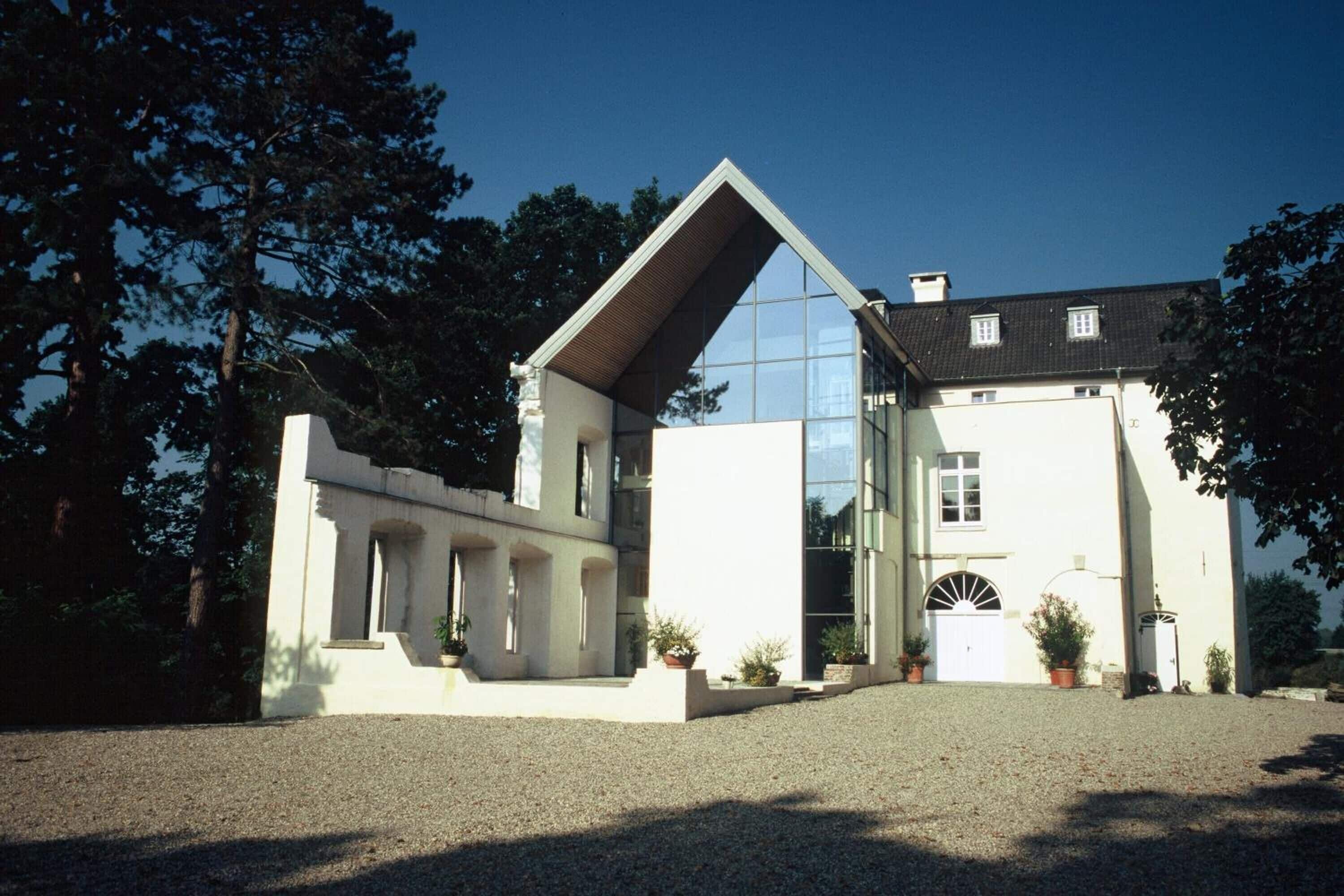 A modern building with a prominent triangular roof, large glass windows, and a gravel driveway.