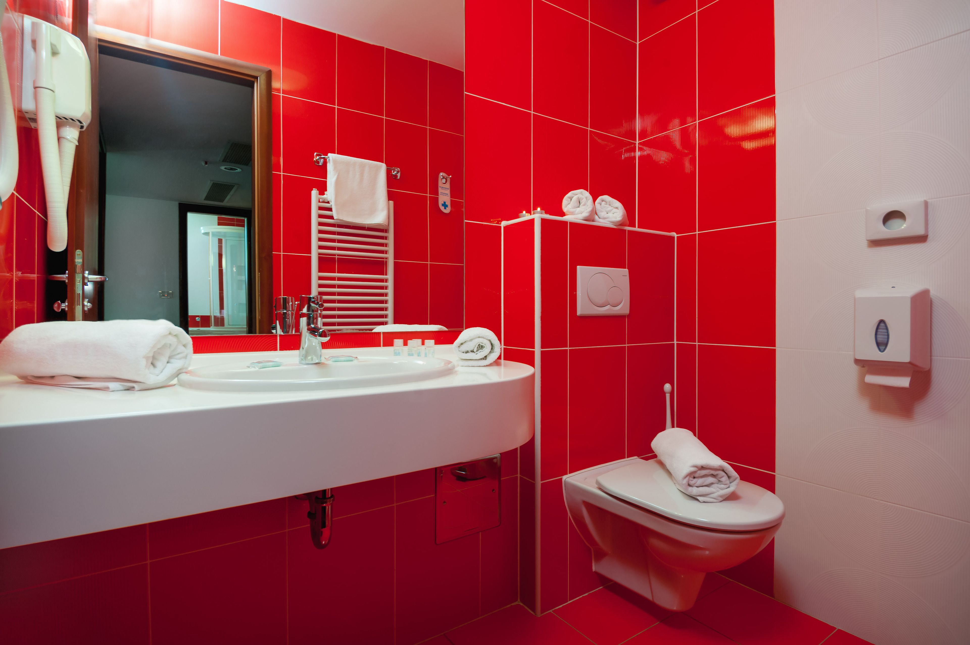 Ein Badezimmer mit roten Fliesen, einem weißen Waschbecken, einem Spiegel, einem Handtuchhalter und einer Toilette.