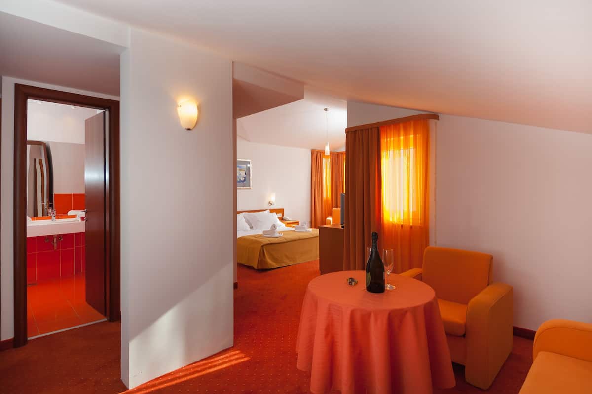 A hotel room with a bed, a table with a bottle and glass, and a chair.