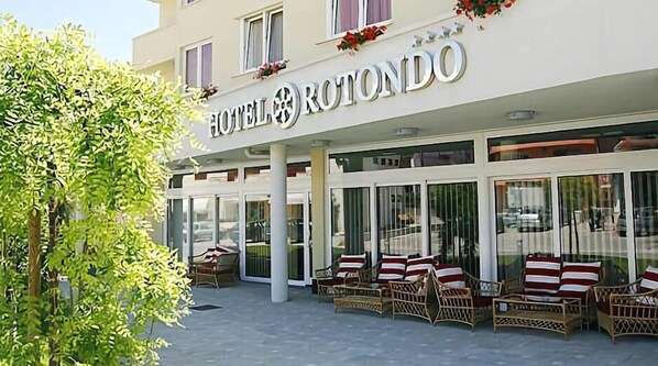 A hotel exterior with a sign reading "HOTEL ROTO NDO". There are wicker chairs with striped cushions outside the entrance.