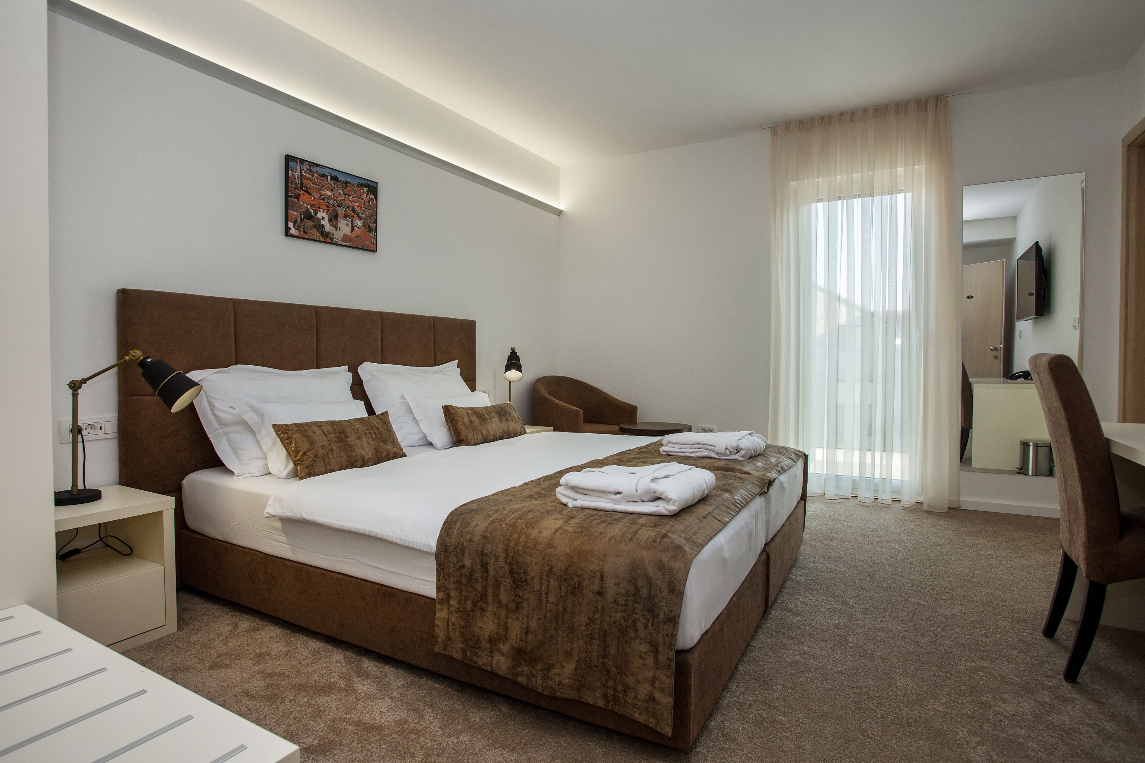 Habitación de hotel con una cama grande, un escritorio, una silla, una mesita de noche y un espejo.
