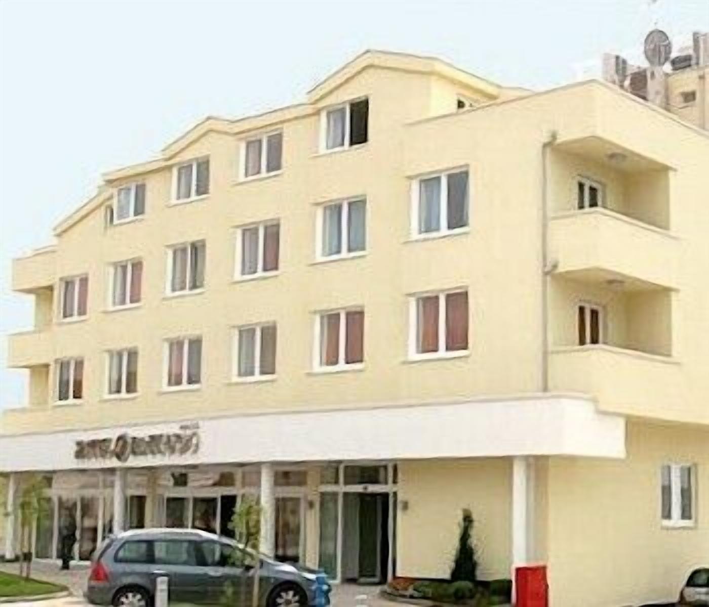 Ένα πολυώροφο ξενοδοχείο με επίπεδη πρόσοψη, πολλά παράθυρα και μια ευδιάκριτη είσοδο, μπροστά στην οποία είναι σταθμευμένο ένα αυτοκίνητο.