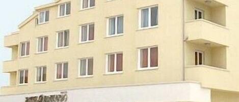 A multi-story hotel with a flat facade, multiple windows, and a visible entrance with a car parked in front.