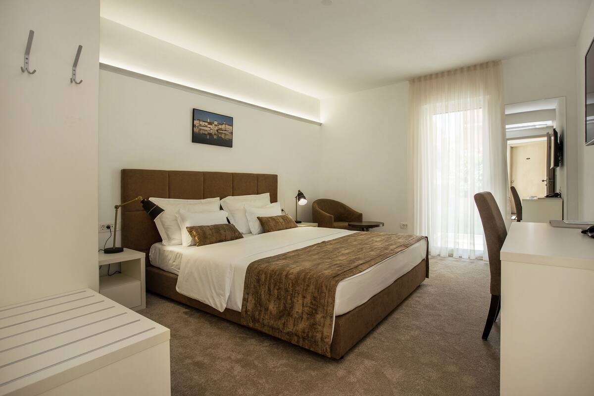 Una habitación de hotel con una cama grande, un escritorio, una silla, una mesita de noche y una lámpara.