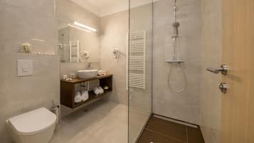 Un baño moderno con ducha de vidrio, lavamanos blanco y tocador con estantes.