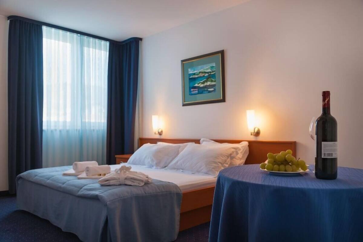 A hotel room with a bed, two bedside tables, a painting on the wall, and a window with curtains.