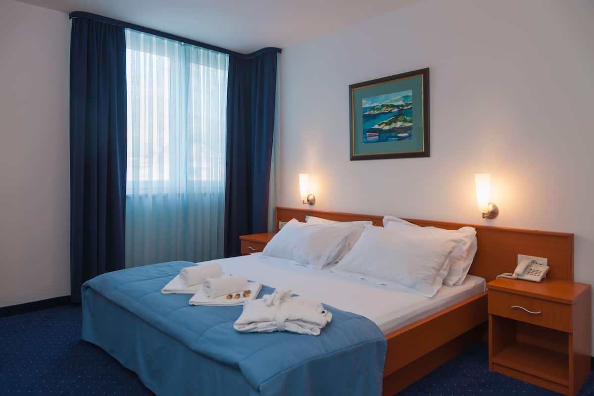 A hotel room with a bed, a nightstand, a telephone, and a painting on the wall.